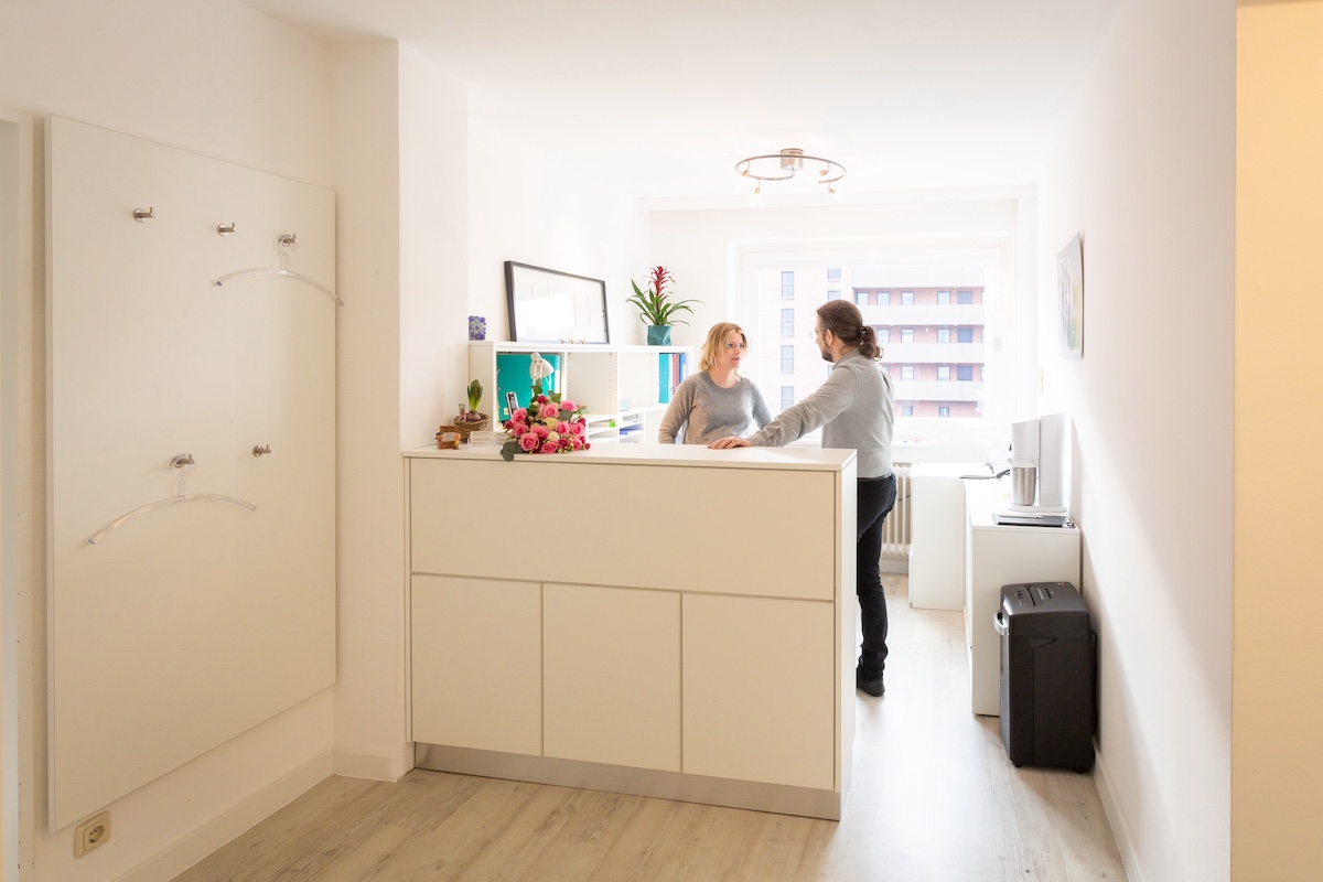 Empfangsbereich – heller Empfangstresen mit Garderobe und Blick in den Flur